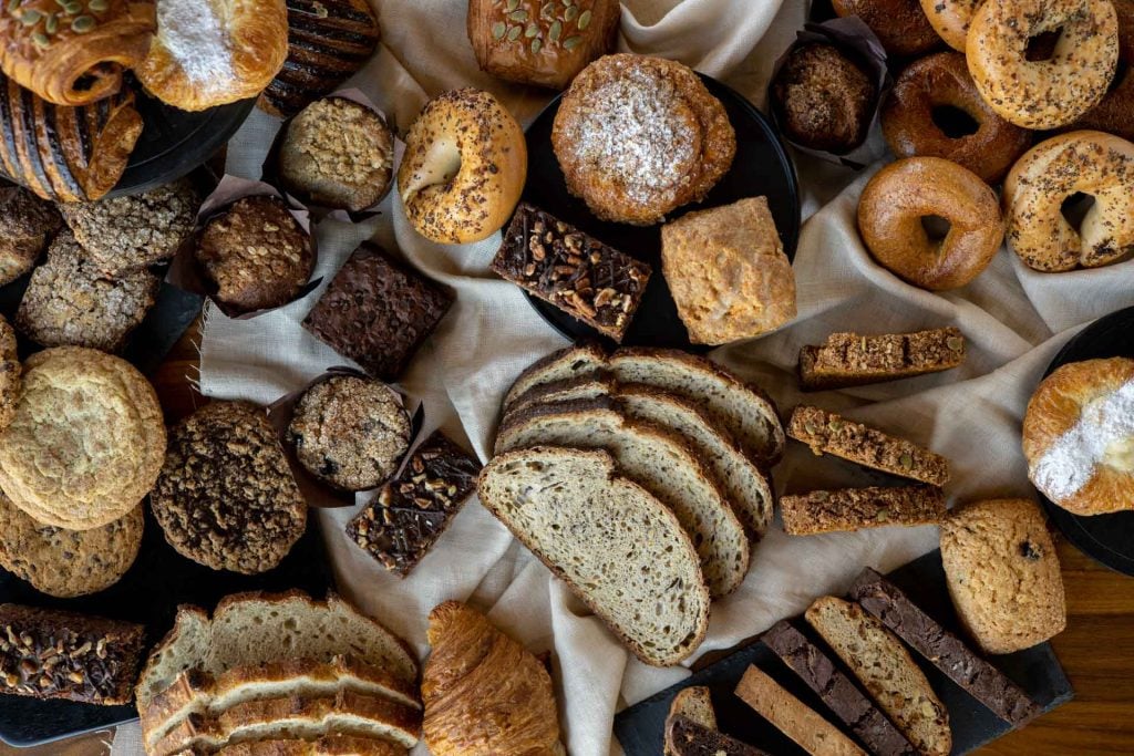 A variety of baked goods on a rustic table, including breads, crackers, and cookies made with diverse grains and ingredients.